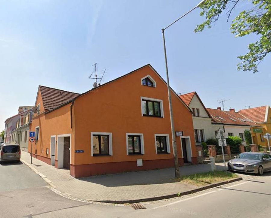 Nárožní dům s cihlově oranžovou fasádou na klidné ulici